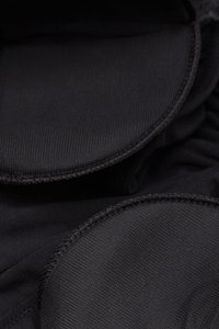 Tissu noir avec une surface texturée, présentant des bords arrondis et des détails de couture. Des sections lisses contrastent avec la texture bosselée.