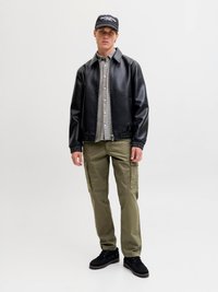Black faux leather jacket with ribbed cuffs, gray checkered shirt underneath, olive green cargo pants, and black shoes. Black cap on head.