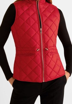 Gilet sans manches matelassé rouge avec fermeture éclair à l'avant, taille à cordon de serrage et poches zippées, porté sur un haut à manches longues noir.