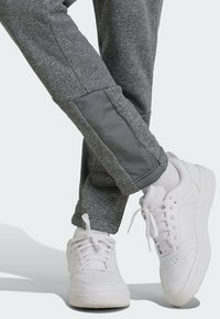 Joggers grises con paneles laterales en gris contrastante, combinados con zapatillas blancas que tienen una parte superior de cuero suave y suela de goma texturizada.