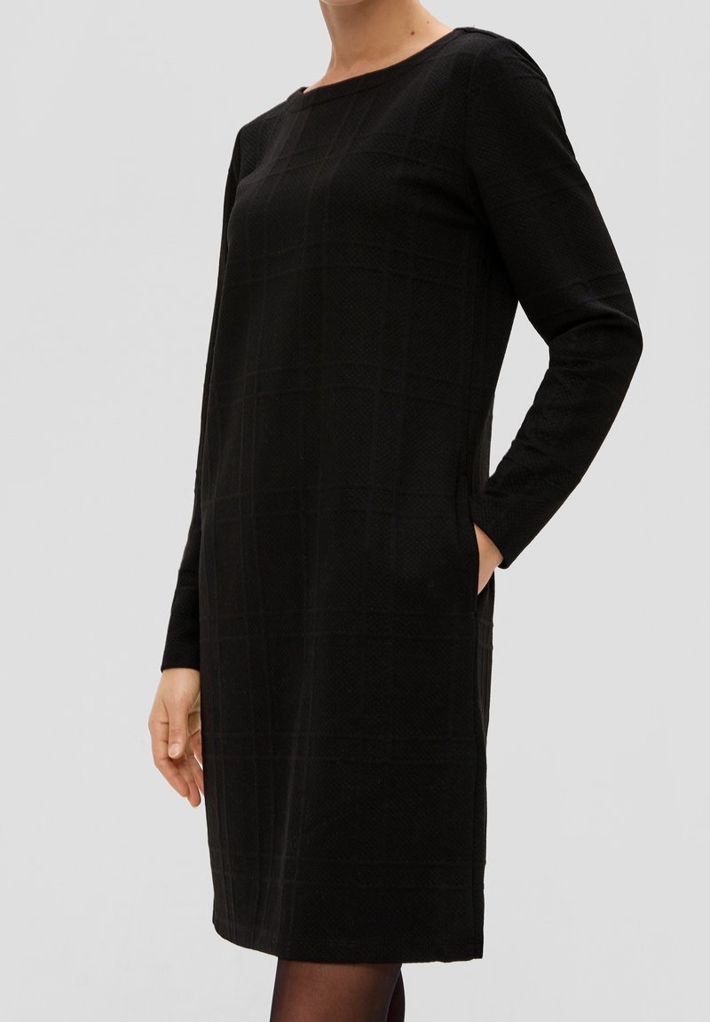 Robe noire à manches longues avec un motif à carreaux texturé, col rond, poches latérales et coupe droite, arrivant à mi-cuisse.