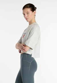 Grijze cropped t-shirt met blauwe en rode tekst. Strak zittende teal leggings met gestructureerde zakken en contrasterende stiksels.