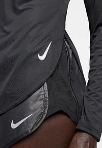 Mustaharjan pitkähihaisen urheilupaidan musta väri, sivuverkko-osa, etupuolella hopeinen Nike-logo ja sileä kangas.