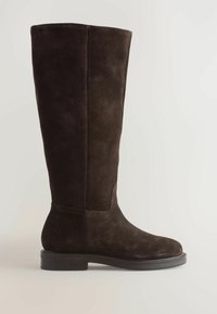 Botă din suede maro, până la genunchi, cu o textură netedă, vârf rotund și o talpă plată, robustă din cauciuc. Prezintă detalii subtile de cusătură.