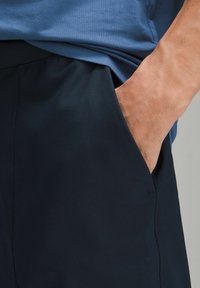 Jūrinės sportinės šortai iš lygaus, lengvo audinio, su šonine kišenę ir elastingu juosmeniu, derinami su mėlynu marškinėliu.