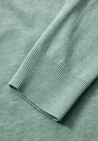 Jasnozielony sweter dzianinowy w zbliżeniu, z ryflowanymi mankietami i gładką teksturą, z miękkim, równym ściegiem na całej powierzchni.