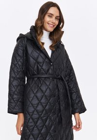 Czarna pikowana kurtka z kapturem, z paskiem w talii, dużymi guzikami i błyszczącą fakturą. Projekt zawiera wzór w romby na całej powierzchni.