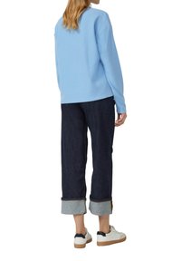 Hellblaues Sweatshirt mit lässiger Passform, kombiniert mit dunklen Jeanshosen mit umgeschlagenen Säumen und weißen Sneakers mit schwarzen Akzenten.