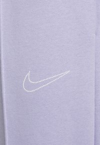Lila sweatpants har en mjuk stickad textur och en vit prickig Nike-logotyp på sidan, vilket ger en minimalistisk design.
