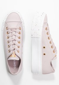 Zapatillas de piel sintética rosa claro con ojales dorados, suelas de goma blanquecina con manchas y cordones planos. Sin patrones prominentes.