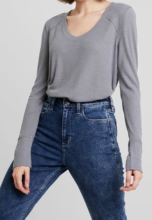Grijze langärmige V-hals top met een ribbelstructuur, gecombineerd met hooggeprijsde vervaagde blauwe jeans met een klassiek vijf-pocket ontwerp.