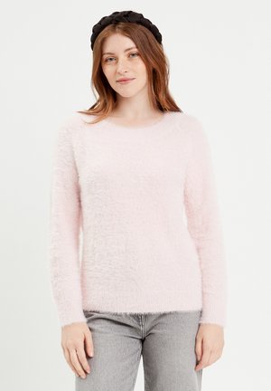 Lichtroze, fluffy trui met lange mouwen en een ronde hals. Zachte textuur en casual pasvorm, gecombineerd met een zwarte haarband.
