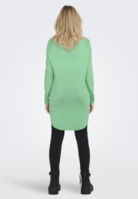 Groene longsleeve top met een relaxte pasvorm, afgeronde zoom en ribbeltextuur, gecombineerd met zwarte skinny broek en stevige zwarte laarzen.