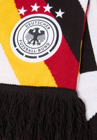 Λογότυπο της Γερμανικής Ποδοσφαιρικής Ομοσπονδίας σε ένα πολύχρωμο κασκόλ με μαύρη φούντα, με διαγώνιες ρίγες σε μαύρο, κόκκινο και κίτρινο χρώμα και τέσσερις λευκές αστερίες.