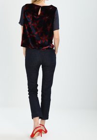 Top negro sin mangas con textura de terciopelo y patrón de estrellas rojas, combinado con jeans oscuros y zapatos de tacón alto rojos con correas en el tobillo.
