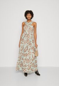 Abito maxi floreale di colore azzurro chiaro, con motivi floreali marroni. Spalline incrociate, silhouette fluida e stivali alla caviglia neri borchiati.