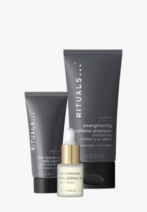 Trzy produkty kosmetyczne: jedna ciemnoszara tubka oznaczona "24h Nawilżający Krem do Twarzy", większa szara tubka na "Wzmacniający Szampon z Kofeiną" oraz biała butelka z pipetą i złotą nakrętką oznaczona "Naturalny Booster Kwas Hialuronowy".