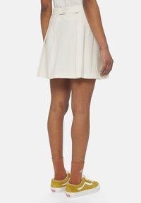 Plissert beige skjørt med en tettsittende midje og knappelukking. Kombinert med gule semsket sneakers og brune ankelstrømper.