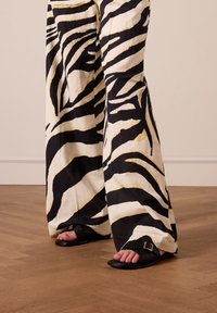 Brede broek met een zwart-wit zebraprint stof, gecombineerd met zwarte gehaakte slippers met een gespsluiting.