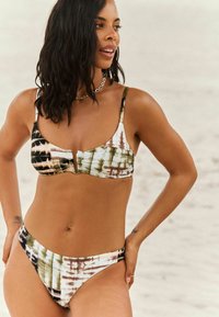 Bikini súprava s pásom v zelených, hnedých a čiernych odtieňoch. Vrchný diel má nastaviteľné ramienka a stredový výrez.