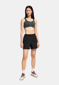 Bermudas atléticas negras y un sujetador deportivo de color verde oscuro, con un diseño ajustado y tejido ligero. Zapatillas beige con acentos en color burdeos.