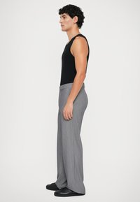 Mannequin die zijwaarts staat, gekleed in een zwart mouwloos shirt, grijze wijde broek en zwarte sneakers tegen een witte achtergrond.