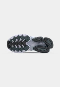 Suola della scarpa con un design contornato e multi-tessuto. Predominantemente grigia con accenti neri e verdi, presenta motivi di battistrada triangolari.