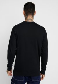 Sudadera negra de manga larga, con un cuello redondo y un acabado texturizado. Presenta una pequeña etiqueta en el dobladillo y un diseño sencillo.