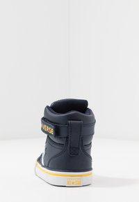 Granatowy sneaker typu high-top z teksturowaną skórzaną cholewką, białą gumową podeszwą, paskiem na rzep oraz żółtym logo "CONVERSE ALL STAR".
