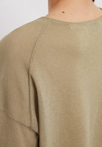 Pull kaki en tissu doux et texturé. Présente un col rond, des coutures discrètes et une coupe décontractée. Montré de dos.
