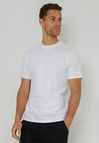 Camiseta blanca de manga corta en textura acanalada con cuello redondo. Combinada con pantalones negros, de corte ajustado y con mínimas costuras.