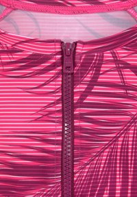 Top atlético rosa con rayas diagonales y un patrón de hojas, que presenta un zipper central en un tono más oscuro de rosa, con textura suave.