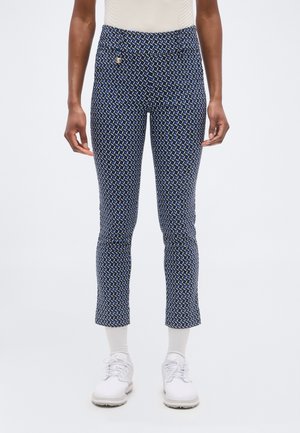 Temno modre hlače s tanko prileganim krojem do gležnjev z vzorcem, nošene z belimi nogavicami in belimi čipkastimi čevlji, prikazane od pasu do nog.