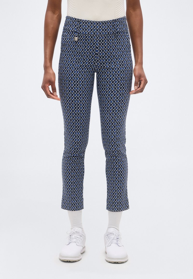 Κομψό παντελόνι σε στενή γραμμή μέχρι τον αστράγαλο, σε σκούρο μπλε με σχέδιο, συνδυασμένο με λευκές κάλτσες και λευκά παπούτσια με κορδόνια, εμφανιζόμενο από τη μέση έως τα πόδια.