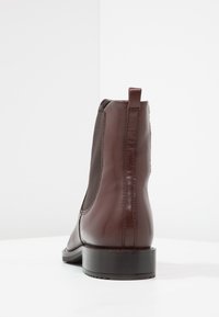 Braunes Leder-Ankle-Boot mit elastischen Seitenpaneelen, glatter Textur, runder Zehenform und einem stabilen schwarzen Absatz. Hinterer Zugriemen für einfaches Anziehen.