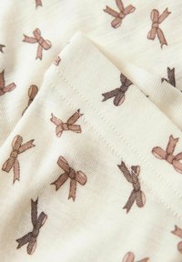 Tissu en coton crème avec un motif de petits nœuds marron. Texture lisse, avec une couture contrastante.