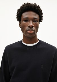 Felpa nera con colletto rotondo e polsini a costine. Presenta un piccolo logo discreto sul lato sinistro del petto. Tessuto con una texture liscia.