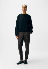 Zwarte gebreide trui met een ronde hals, gecombineerd met slim-fit donkerbruine broeken en zwarte leren schoenen. Eenvoudig, textuurvol ontwerp.