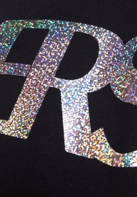 Tela negra con letras holográficas grandes y brillantes en plateado, que muestran efectos de purpurina de colores del arcoíris a través de la superficie.