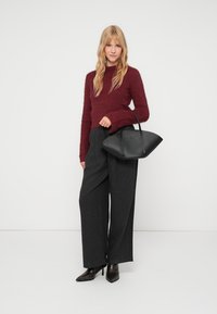 Bordo puhast pulover, črne hlače z visoko pasom in širokimi nogavicami ter strukturirana črna torbica. Model nosi črne čevlje s koničastim prstom do gležnja.