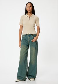 Polo de rayas beige con mangas cortas y tapeta de botones; vaqueros de pierna ancha azul claro con un ligero desgaste; zapatos de tacón blancos.
