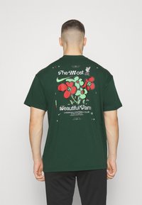 Ciemnozielona bawełniana koszulka z graficznym nadrukiem czerwonych kwiatów oraz tekstem "Najpiękniejsza gra" i "Liverpool Football Club" z tyłu.