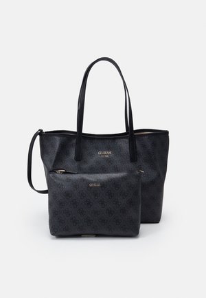 Sac cabas noir Guess avec pochette zippée assortie, tous deux présentant un logo à motif subtil et un marquage Guess doré sur le devant.