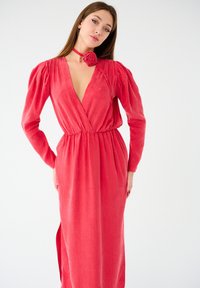 Robe rouge à manches longues avec un décolleté en V, taille froncée et fente latérale. Fabriquée dans un tissu doux avec une finition texturée. Inclut un choker floral assorti.
