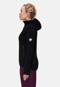 Black hooded jacket with a fitted design, long sleeves, a zippered pocket, and a logo on the left arm. Textured fabric.