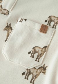 Bawełniana koszula z kremowym tłem i powtarzającym się nadrukiem osła. Zawiera teksturowaną kieszeń z akcentem z brązowej skórzanej metki.