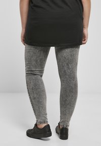 Szürke farmer leggings, elhalványult, textúrált mintával, fekete tornacipővel párosítva. A felső egy hosszú fekete póló, amely részben eltakarja a leggingset.