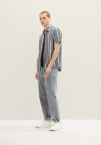 Kortærmet, navy stribet skjorte med en afslappet pasform, parret med lysegrå jeans og hvide sneakers. Glat stof, afslappet design.