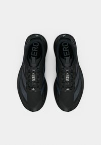 Ténis desportivos pretos com design elegante, apresentando tecido texturizado, detalhes em cinza escuro e atacadores proeminentes, evidenciando uma estrutura leve.