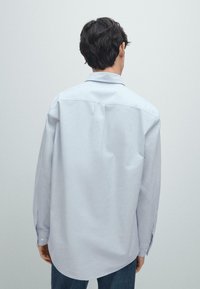 Jasnoniebieska koszula z długim rękawem o luźnym kroju i zaokrąglonym dołem. Gładki materiał o subtelnej fakturze, z guzikami przy mankietach.